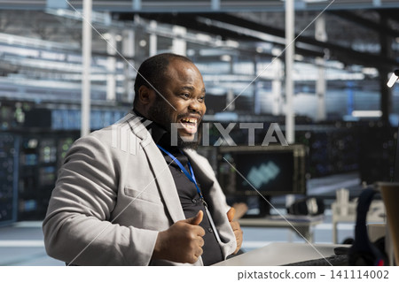 Delighted coder in server facility satisfied by improved system efficiency metrics. Ecstatic African American man working in server facility satisfied by enhanced network infrastructure performance. Delighted coder in server facility satisfied by improved system efficiency metrics. Ecstatic African American man working in server facility satisfied by enhanced network infrastructure performance. 141114002
