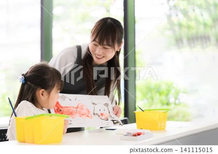 一位大約小學年齡的小女孩在美術課上畫水彩畫,她的母親和老師在一旁觀看——這是一段培養創造力的親子教育時光。 一位大約小學年齡的小女孩在美術課上畫水彩畫,她的母親和老師在一旁觀看——這是一段培養創造力的親子教育時光。 141115015