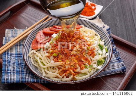 lifting Shaanxi hand-pulled noodles with chopsticks from a bowl, featuring spicy chili and sausage topping, close-up shot 141116062