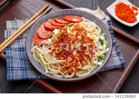 lifting Shaanxi hand-pulled noodles with chopsticks from a bowl, featuring spicy chili and sausage topping, close-up shot lifting Shaanxi hand-pulled noodles with chopsticks from a bowl, featuring spicy chili and sausage topping, close-up shot 141116063