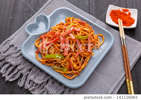 stirred Chinese spicy hand-pulled noodles with ham and green peppers on a blue ceramic plate with chili powder on the side stirred Chinese spicy hand-pulled noodles with ham and green peppers on a blue ceramic plate with chili powder on the side 141116065