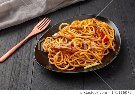 authentic Xinjiang style stir-fried hand-pulled noodles with beef and vegetables on a green plate, rustic white wood background authentic Xinjiang style stir-fried hand-pulled noodles with beef and vegetables on a green plate, rustic white wood background 141116072