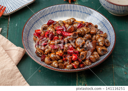 a plate of stir-fried river snails with dried chilies and wooden spoon, rustic style Chinese food background. a plate of stir-fried river snails with dried chilies and wooden spoon, rustic style Chinese food background. 141116251