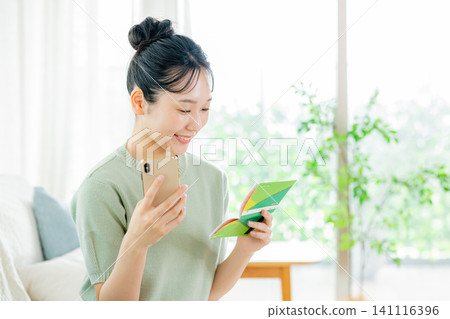 A young woman looking at her smartphone and bankbook A young woman looking at her smartphone and bankbook 141116396