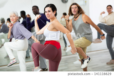 Happy young woman practising modern dance moves with other people in dance studio Happy young woman practising modern dance moves with other people in dance studio 141116629