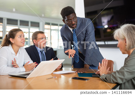 Angry middle-aged man shouting at his business partners sitting around table Angry middle-aged man shouting at his business partners sitting around table 141116694