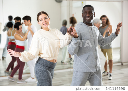 Happy african-american guy and caucasian girl practising paired latin dance in dance studio Happy african-american guy and caucasian girl practising paired latin dance in dance studio 141116698