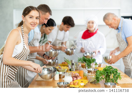 Enthusiastic young woman engrossed in cooking at group culinary class Enthusiastic young woman engrossed in cooking at group culinary class 141116738