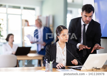 Adult man helping young female colleague work on laptop Adult man helping young female colleague work on laptop 141116978