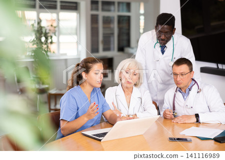 Doctors sitting around the table looking at the notebook Doctors sitting around the table looking at the notebook 141116989