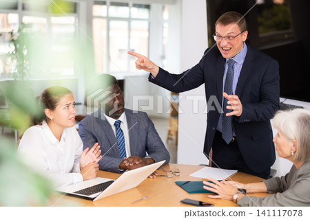 Angry middle-aged man shouting at his business partners sitting around table Angry middle-aged man shouting at his business partners sitting around table 141117078