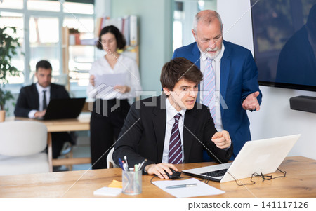 Elderly man helping young male colleague work on laptop Elderly man helping young male colleague work on laptop 141117126