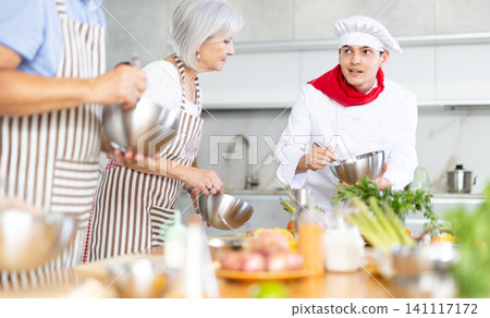 Cooking class, food and people concept - happy group of friends and male chef cook cooking in kitchen Cooking class, food and people concept - happy group of friends and male chef cook cooking in kitchen 141117172