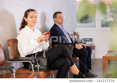 Serious-minded female candidate siting on chair and waiting for job interview in hallway Serious-minded female candidate siting on chair and waiting for job interview in hallway 141117174