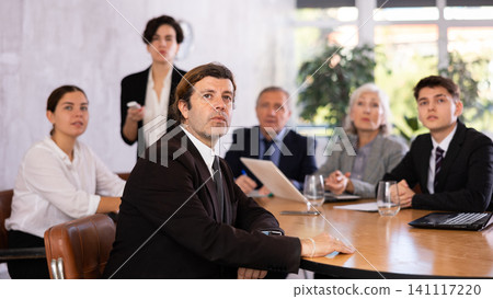 Concentrated young adult old office workers sitting around the table and looking at screen while Latin female using projector remote control in office Concentrated young adult old office workers sitting around the table and looking at screen while Latin female using projector remote control in office 141117220