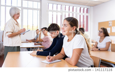 Young girl listening to lecture and taking notes in classroom Young girl listening to lecture and taking notes in classroom 141117228