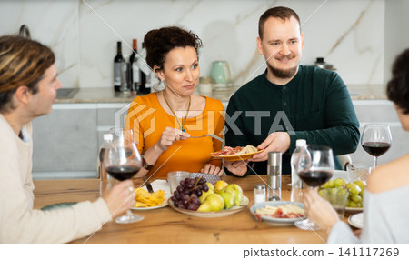 Two married couples are sitting at table, enjoying food and wine, chatting, talking, laughing. 141117269