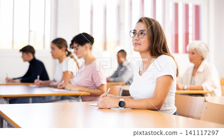 Young Hispanic woman listening to lecture and taking notes in classroom 141117297