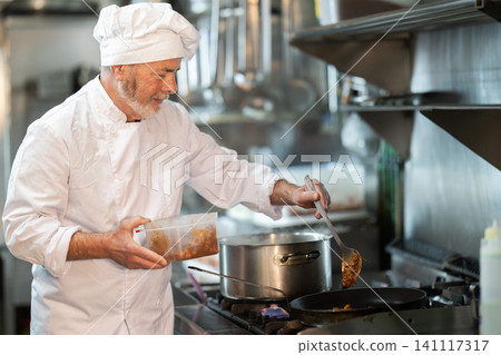 Mature man cook in kitchen is working near stove Mature man cook in kitchen is working near stove 141117317