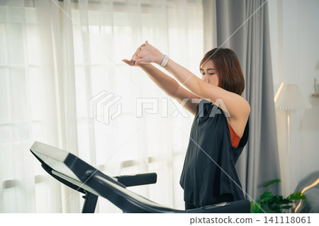Young woman stretching arm muscles before treadmill workout at home Young woman stretching arm muscles before treadmill workout at home 141118061