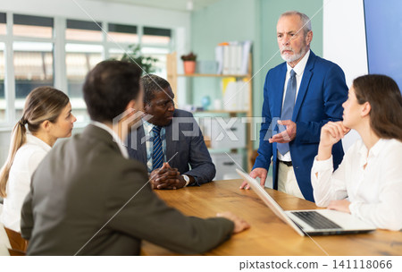 Mature man stands in front of business colleagues, tells report Mature man stands in front of business colleagues, tells report 141118066