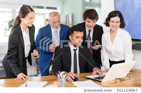 Group of business people discuss business strategies and planning work together, everyone looking at laptop by man and laughing in corporate office 141118067