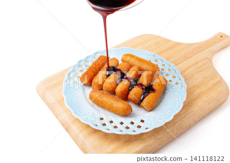 pouring dark brown sugar syrup onto crispy fried glutinous rice cakes on a light blue plate and wooden cutting board 141118122