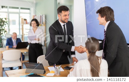 Friendly adult male bank manager offering to shake hand with young couple of clients at office 141118172