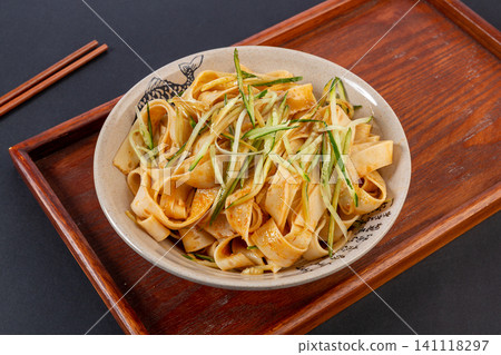 spicy cold dried mianpi wheat noodles with shredded cucumber served on a wooden tray spicy cold dried mianpi wheat noodles with shredded cucumber served on a wooden tray 141118297