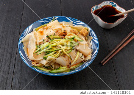 traditional Chinese Shaanxi mixed Liangpi cold noodle salad with chili oil sauce on a dark wooden table traditional Chinese Shaanxi mixed Liangpi cold noodle salad with chili oil sauce on a dark wooden table 141118301