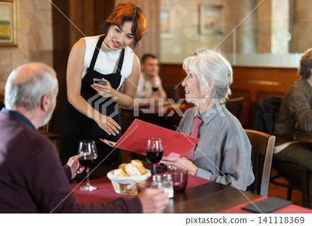 Young waitress taking order from elderly couple in restaurant 141118369