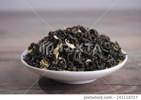 Dried jasmine green tea leaves in a white ceramic bowl on a wooden table Dried jasmine green tea leaves in a white ceramic bowl on a wooden table 141118727