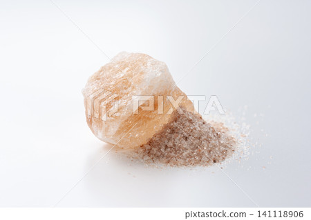 A chunk of pink rock salt and fine salt grains placed against a white background. 141118906