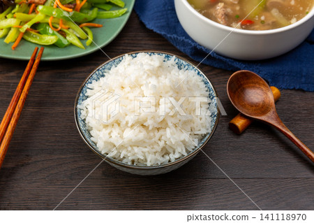 A bowl of freshly cooked fluffy white rice in a traditional ceramic bowl with chopsticks on a rustic wooden table. A bowl of freshly cooked fluffy white rice in a traditional ceramic bowl with chopsticks on a rustic wooden table. 141118970