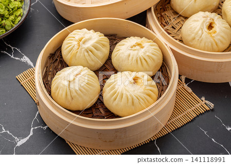 Chinese steamed pork buns (Baozi) inside a traditional bamboo steamer on a dark marble background. 141118991