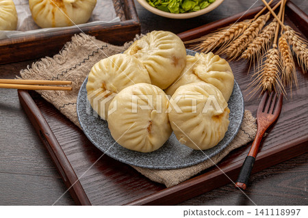 Traditional Chinese breakfast steamed meat buns served on a ceramic plate with rustic wooden decor. 141118997