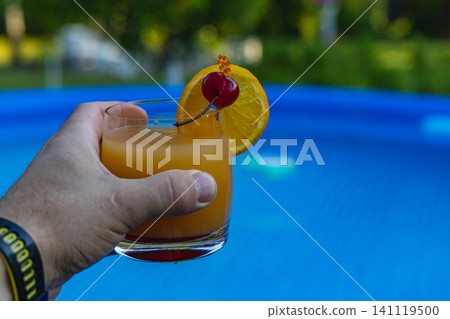 Refreshing cocktail with orange and cherry by the pool on a sunny day Refreshing cocktail with orange and cherry by the pool on a sunny day 141119500