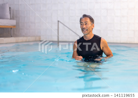 A smiling senior man doing water walking in a swimming pool. A smiling senior man doing water walking in a swimming pool. 141119655