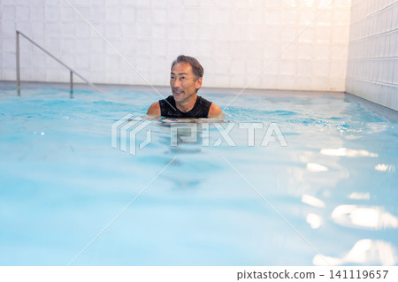 A smiling senior man doing water walking in a swimming pool. A smiling senior man doing water walking in a swimming pool. 141119657