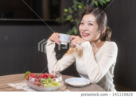 一位微笑的年輕女子正在放鬆地喝咖啡。 一位微笑的年輕女子正在放鬆地喝咖啡。 141119828