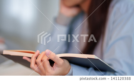 Adult woman holding open book while studying in blurred educational environment with copy space 141120388