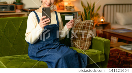 A woman sitting on a sofa with her smartphone and card. A woman sitting on a sofa with her smartphone and card. 141121604