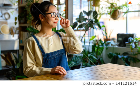 A woman in her 30s touching her glasses on a table. A woman in her 30s touching her glasses on a table. 141121614
