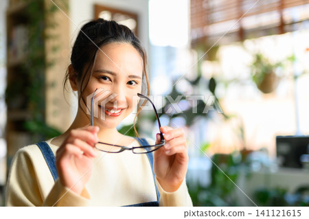 一位年輕的日本女子麵帶微笑,手中拿著眼鏡。 一位年輕的日本女子麵帶微笑,手中拿著眼鏡。 141121615