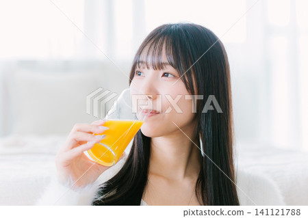 一位年輕女子在房間裡喝著柳橙汁 一位年輕女子在房間裡喝著柳橙汁 141121788