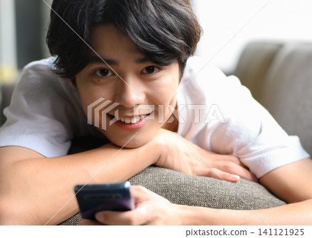 A man sitting on a sofa with his smartphone A man sitting on a sofa with his smartphone 141121925