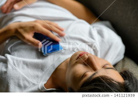 一個男人睡在沙發上,旁邊是他的智慧型手機 一個男人睡在沙發上,旁邊是他的智慧型手機 141121939