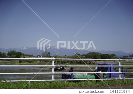 A spring rural landscape with snow-capped mountains in the distance, people working in the fields, and a light truck. A spring rural landscape with snow-capped mountains in the distance, people working in the fields, and a light truck. 141121984