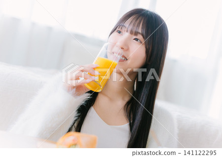 一位年輕女子在房間裡喝著柳橙汁 一位年輕女子在房間裡喝著柳橙汁 141122295