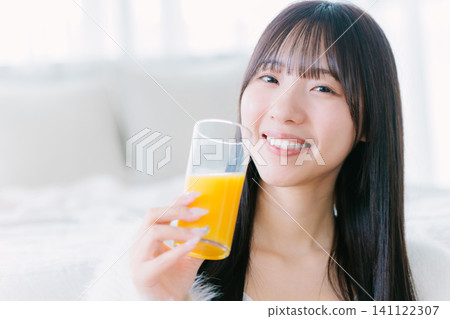 A young woman drinking orange juice in her room 141122307